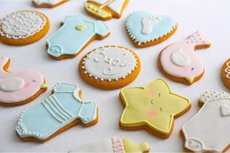 Decorated baby shower biscuits shaped like baby clothes, birds and stars in pastel colours.