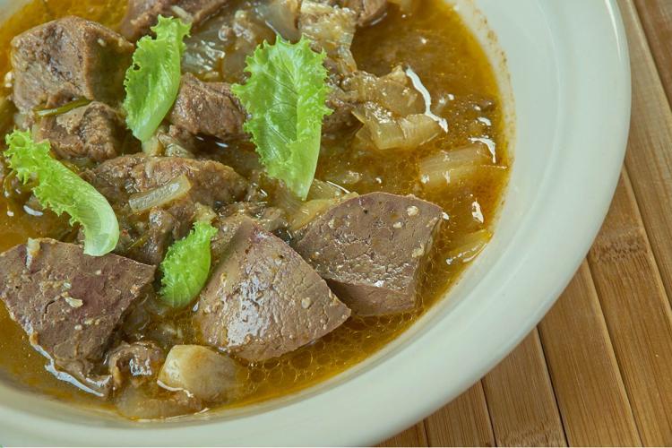Bowl of kamounia, chunks of liver and beef with onion in a cumin-spiced broth, garnished with lettuce leaves