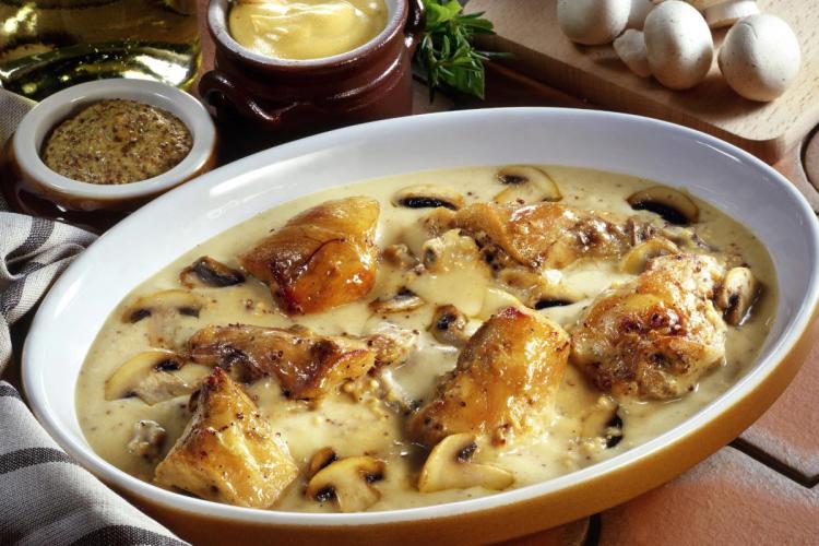 Pieces of rabbit in a creamy mustard and mushroom sauce in a white oval dish, with pots of Dijon and wholegrain mustard alongside