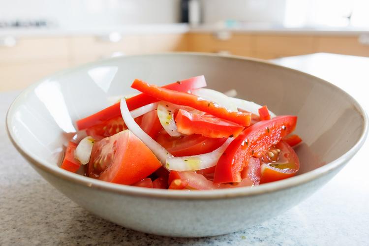 A bowl of Argentine tomato and onion salad with red bell pepper strips, dressed with olive oil and oregano