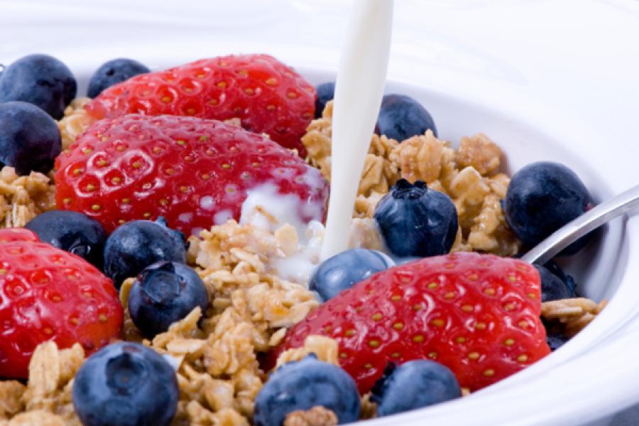 Pouring milk on breakfast granola, strawberries and blueberries.