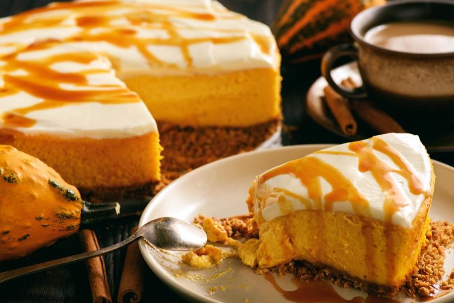 A plate with a slice of pumpkin cheesecake with the rest of the cake on the background.