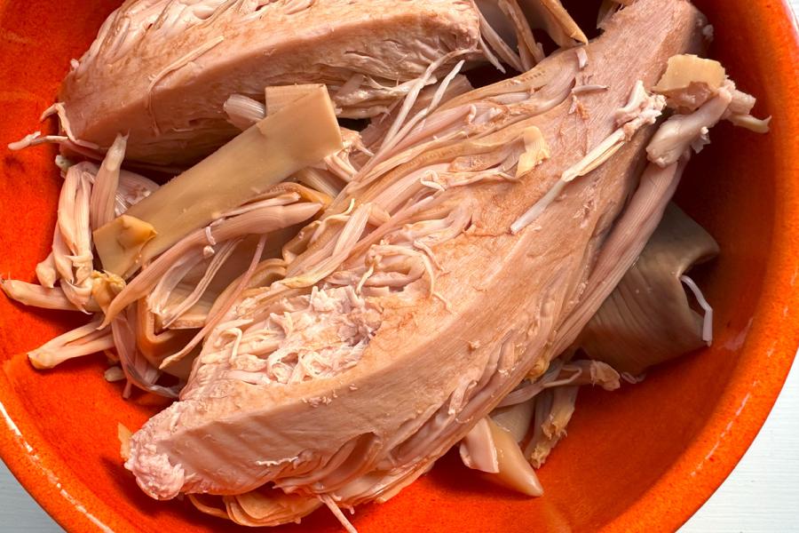 Close-up view of canned banana blossom in an orange bowl, showing the fibrous, shredded texture of the blossom pieces.