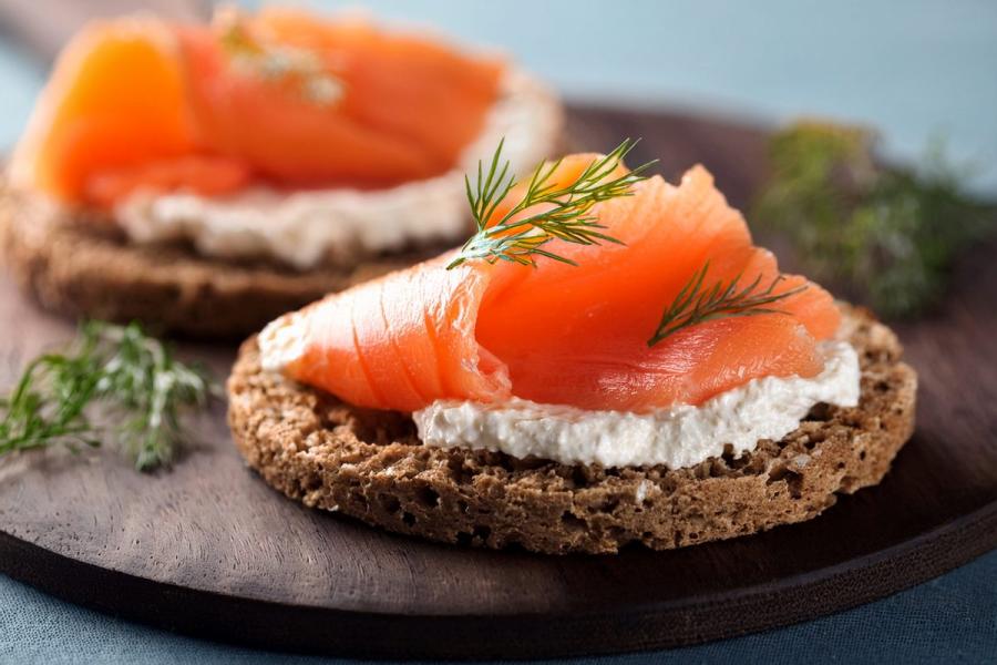 Smoked salmon canapé on rustic soda bread with creamy cheese, garnished with fresh dill, served on a dark wooden board - AIG.