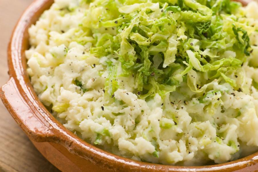 A traditional Irish dish made of mashed potatoes mixed with finely chopped cabbage. The dish is served in a rustic ceramic bowl and sprinkled with black pepper.