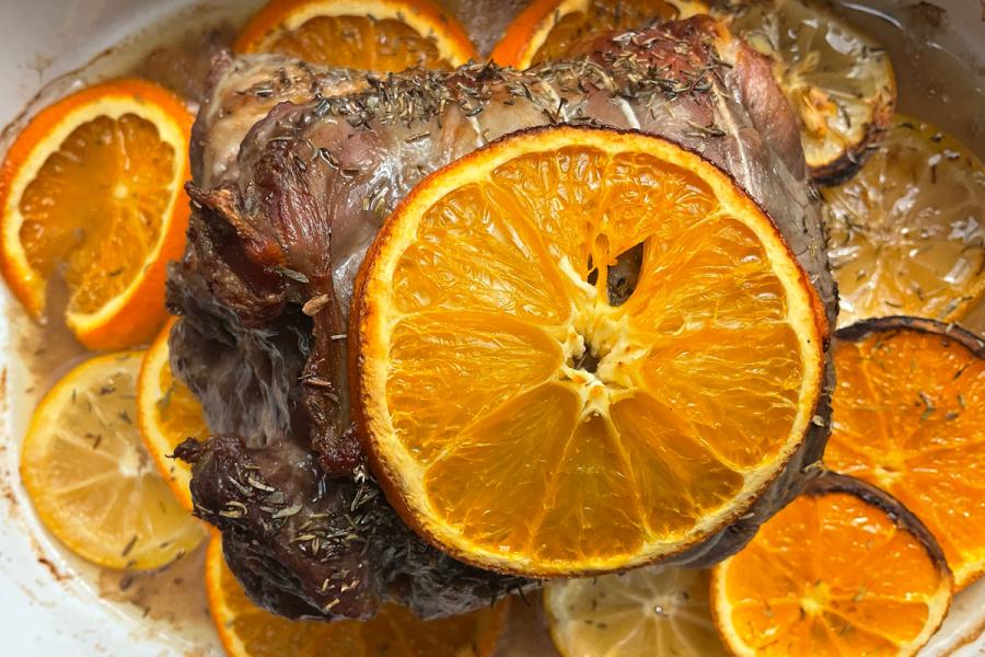 Slow-roasted lamb with thyme, fresh orange and lemon slices in a white baking dish, St Clement’s roast lamb dish with citrus and herbs.
