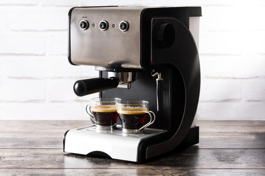 Modern espresso machine brewing two shots of espresso into glass cups on a wooden surface with a white brick wall background.