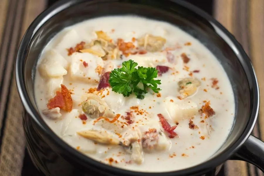 Bowl of New England clam chowder with potatoes, clams, and bacon, garnished with parsley.