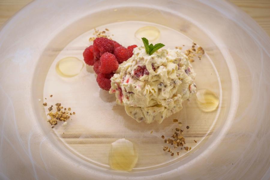 A portion of cranachan served on a plate with fresh raspberries and mint leaves with drops of honey and crumbled toasted oats as decoration.