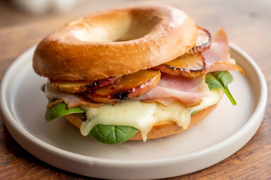 Bagel sandwich with ham, melted cheese, spinach, and grilled apple slices on a ceramic plate.