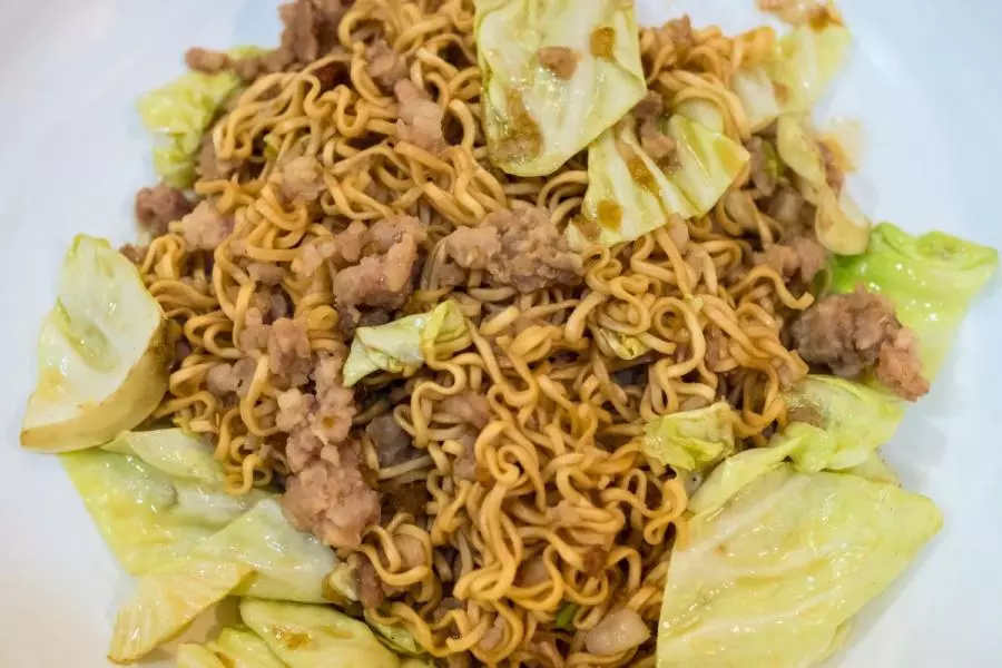 Stir-fried noodles with pork and cabbage on a white plate.