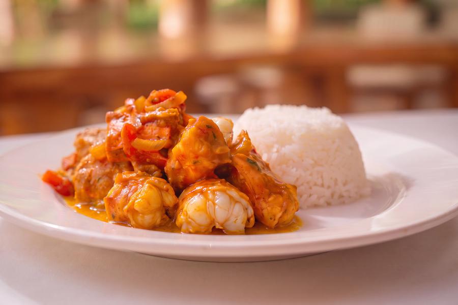 Chunks of lobster tail in a thick orange curry sauce with onion and red pepper, served beside a moulded dome of white rice on a white plate