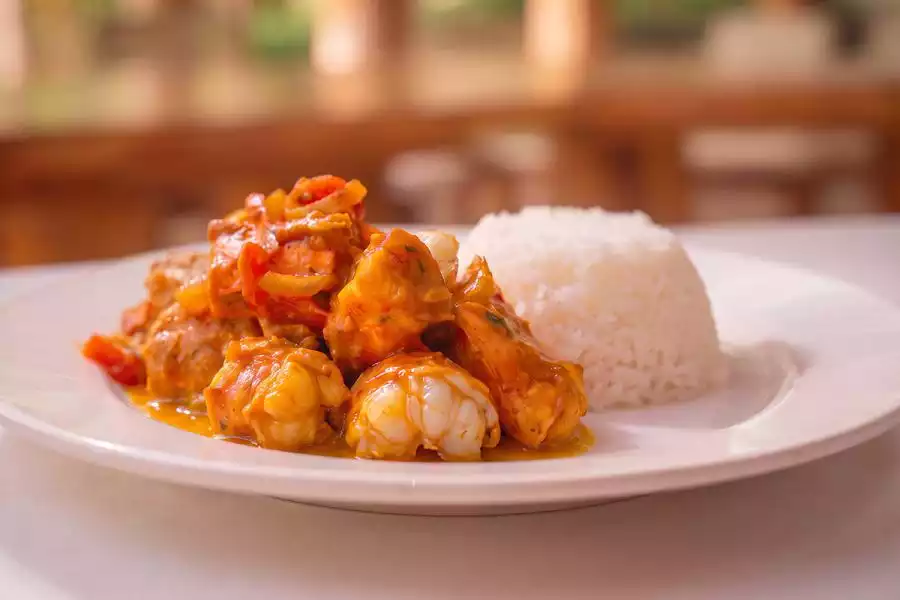 Chunks of lobster tail in a thick orange curry sauce with onion and red pepper, served beside a moulded dome of white rice on a white plate