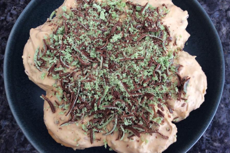 Overhead view of a whole peppermint and chocolate tart on a dark plate, generously topped with green mint chocolate and dark chocolate shavings.
