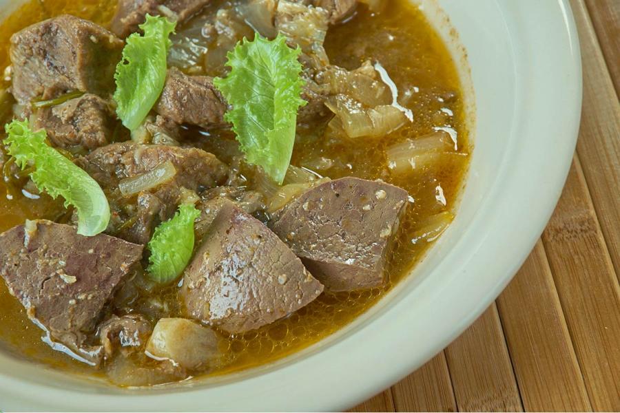 Bowl of kamounia, chunks of liver and beef with onion in a cumin-spiced broth, garnished with lettuce leaves