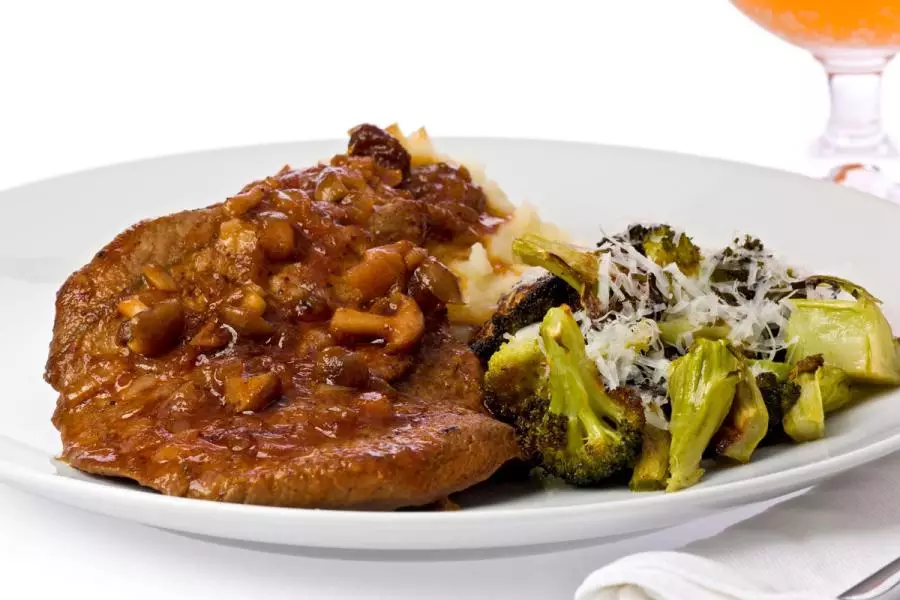 A pan-fried steak topped with a rich mushroom and onion sauce, served with mashed potatoes and parmesan-topped roasted broccoli and bok choy.
