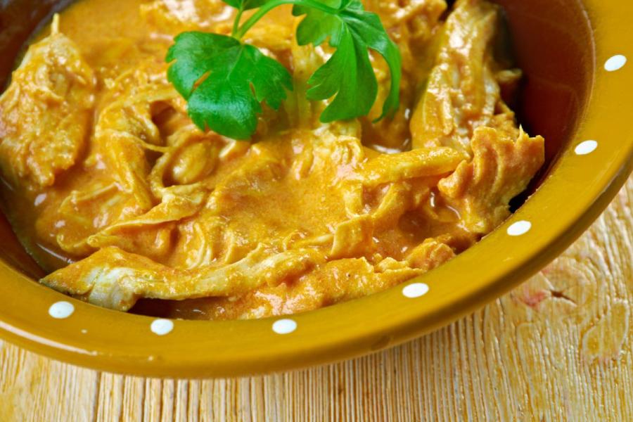 Bowl of shredded chicken in a creamy orange palm-nut sauce, garnished with parsley, in a yellow polka-dot dish