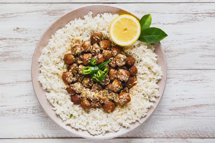 A plate of Egyptian shrimp kofta — small golden-fried shrimp croquettes sprinkled with sesame seeds and herbs — arranged over a ring of white rice and topped with sliced green chile and half a lemon.