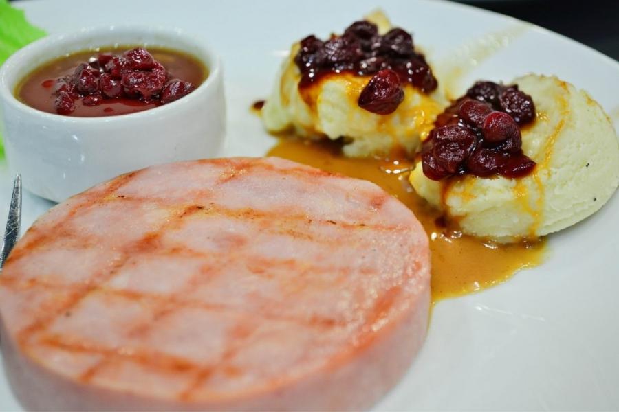 A ham steak with mashed potato and cherry sauce.
