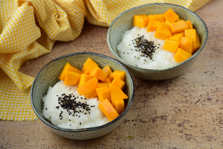 Two bowls with mango sticky rice decorate with toasted black sesame seeds.