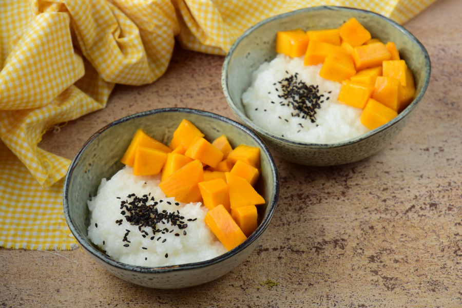 Two bowls with mango sticky rice decorate with toasted black sesame seeds.