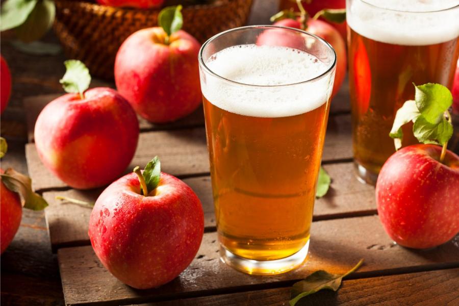 Two glasses of cider surrounded by apples.