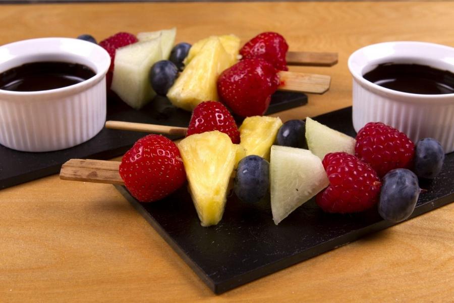 Two fresh fruit kebabs accompanied with small bowls of melted chocolate.