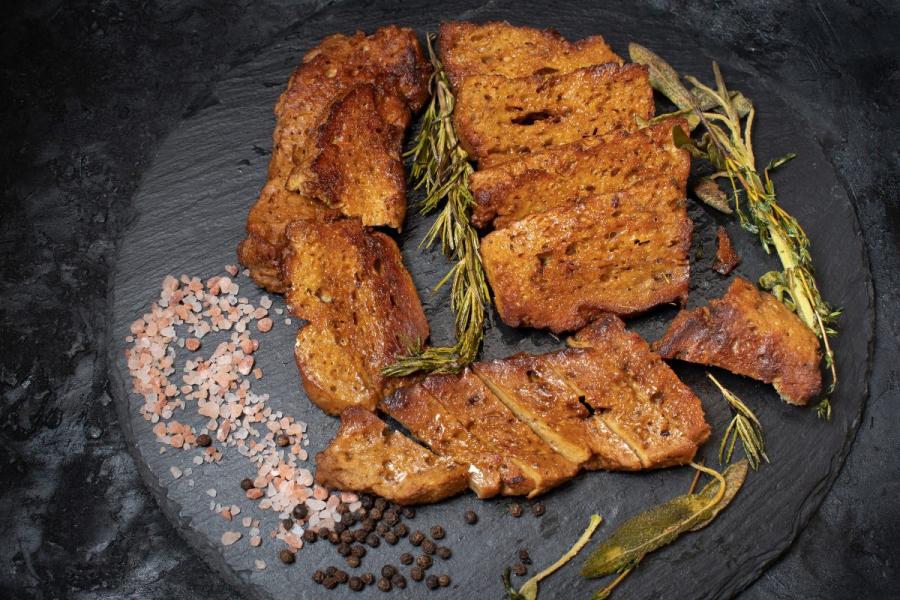 Roasted seitan steaks with rosemary, pink salt and black pepper on a slate plate.