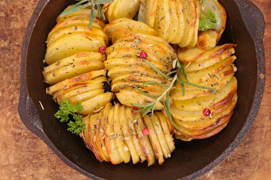 A cast iron pan with baked sliced potatoes decorated with herbs and pink pepper.