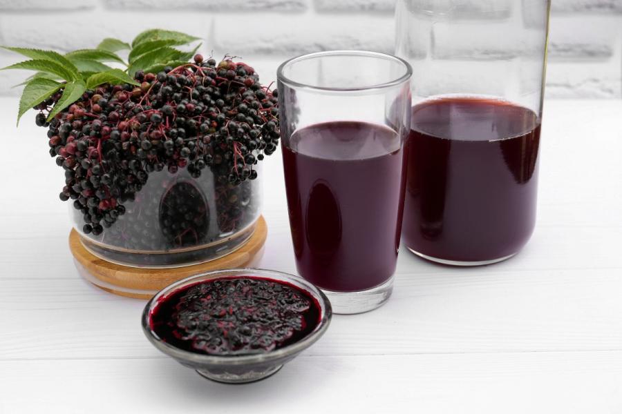 Two glasses of elderberry wine, elderberry jam and some fresh elderberries.
